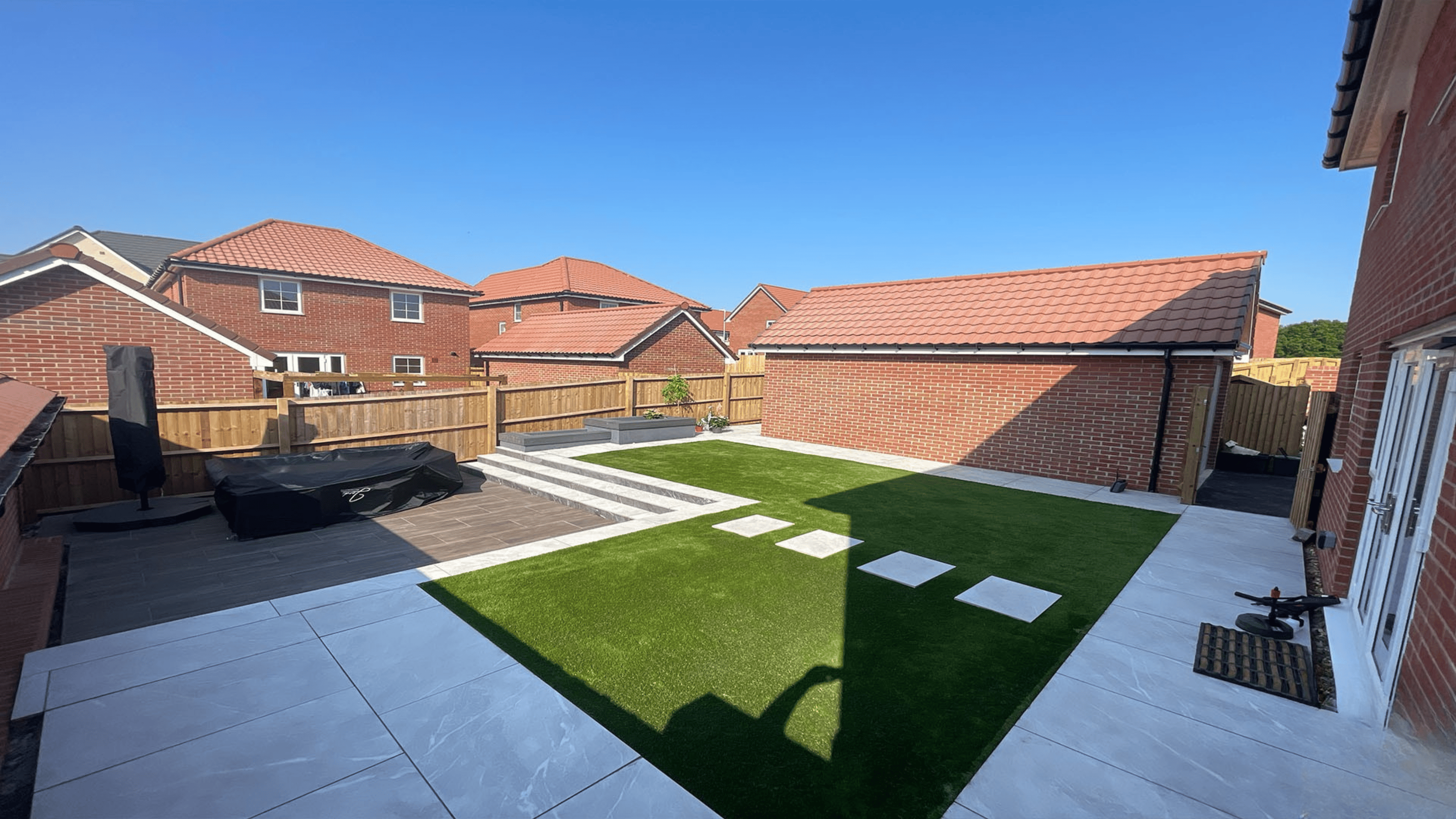 Contemporary garden with a large paved patio, raised wooden planters, and lush green lawn, designed for outdoor entertaining in Bristol