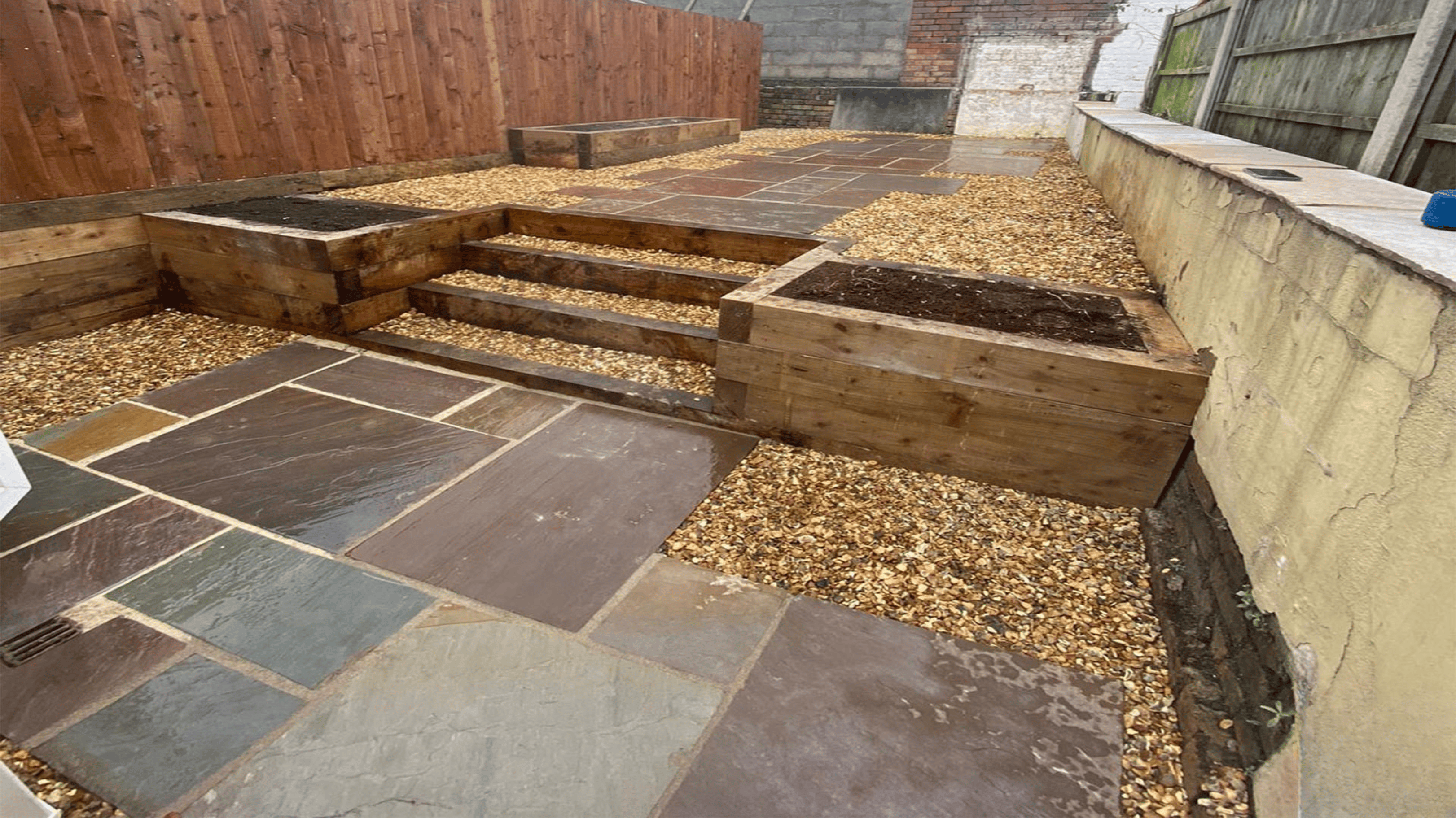Contemporary garden with a large paved patio, raised wooden planters, and lush green lawn, designed for outdoor entertaining in Bridgwater